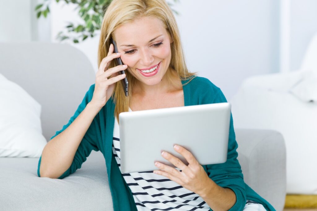 A lovely woman talks on the phone with her med spa provider while looking at her computer tablet. She's scheduling a treatment with the med spa, showing why lead follow-up is critical to their private practice’s success.