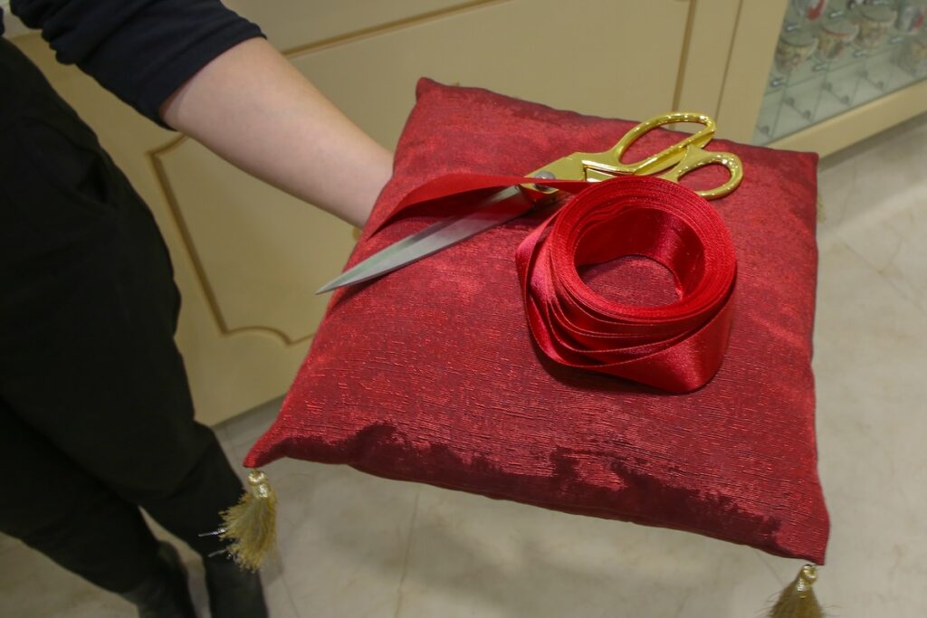 A provider's hand holding a velvet pillow with golden scissors and a red ribbon, preparing for their grand opening. They've gotten ready through hard work and by taking advice about opening your private practice.